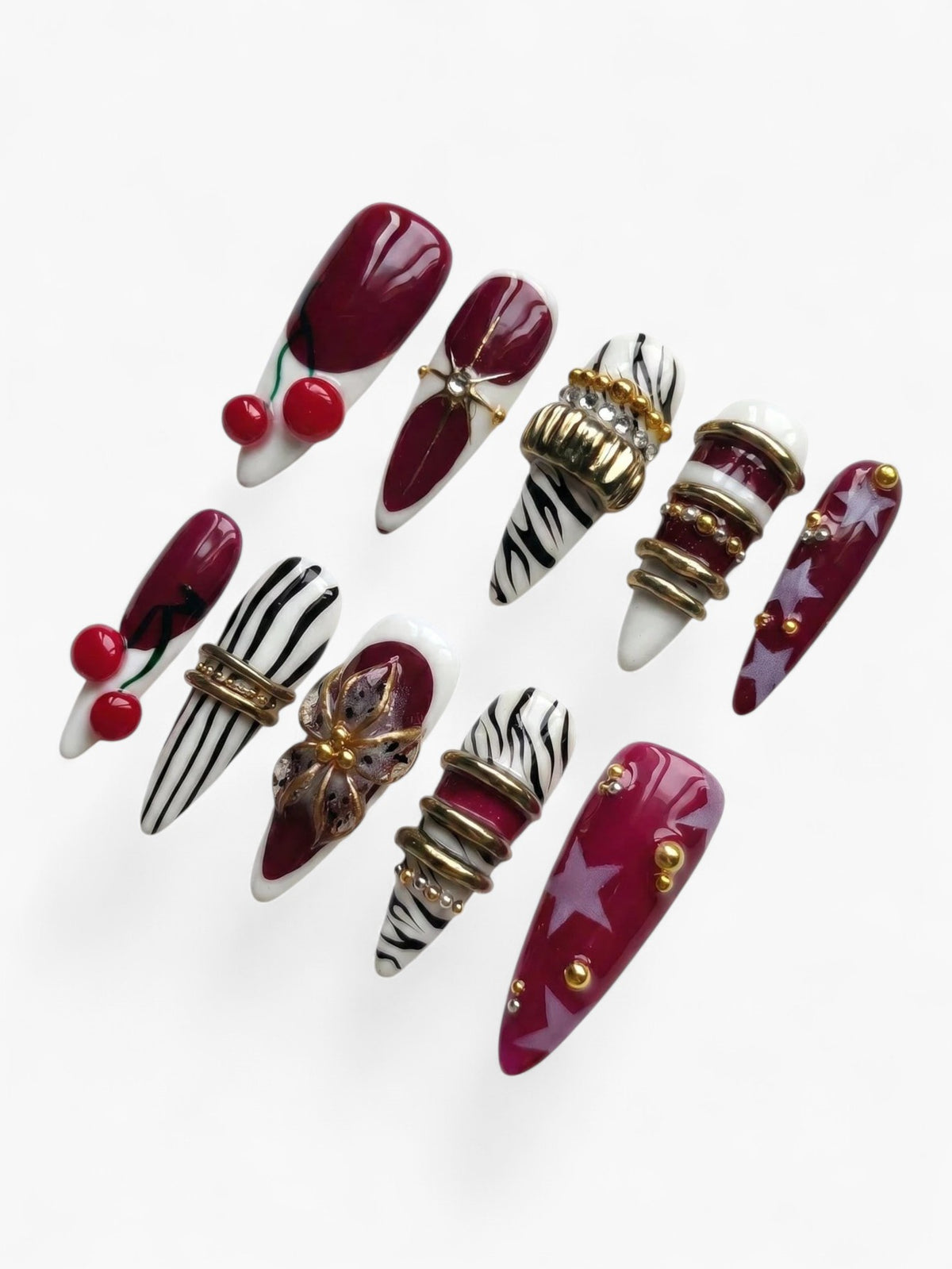 Cherry Rouge Cherry Mirage, faux ongles en amande rouge cerisier et bordeaux avec motifs zébrés, étoiles et bijoux dorés