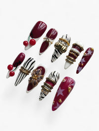 Cherry Rouge Cherry Mirage, faux ongles en amande rouge cerisier et bordeaux avec motifs zébrés, étoiles et bijoux dorés