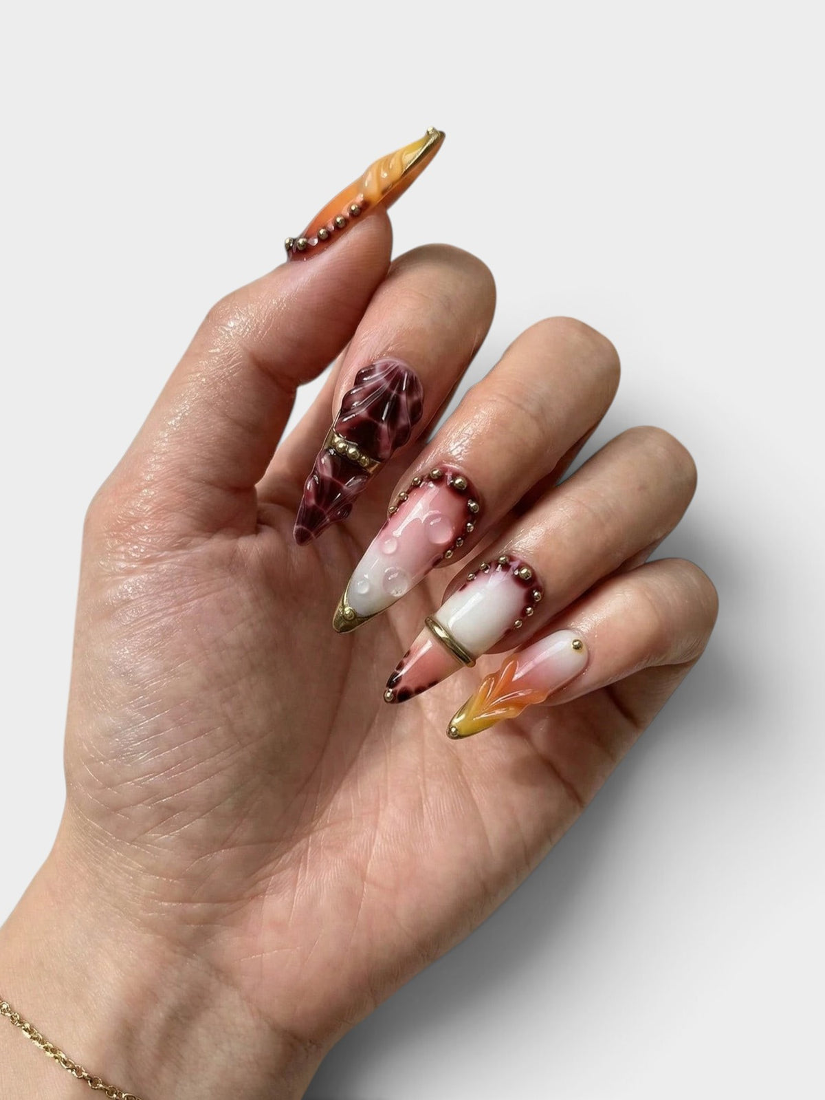 Main Cherry Rouge ornée de faux ongles en amande longs, dégradé rouge crimson et vin avec détails en relief dorés