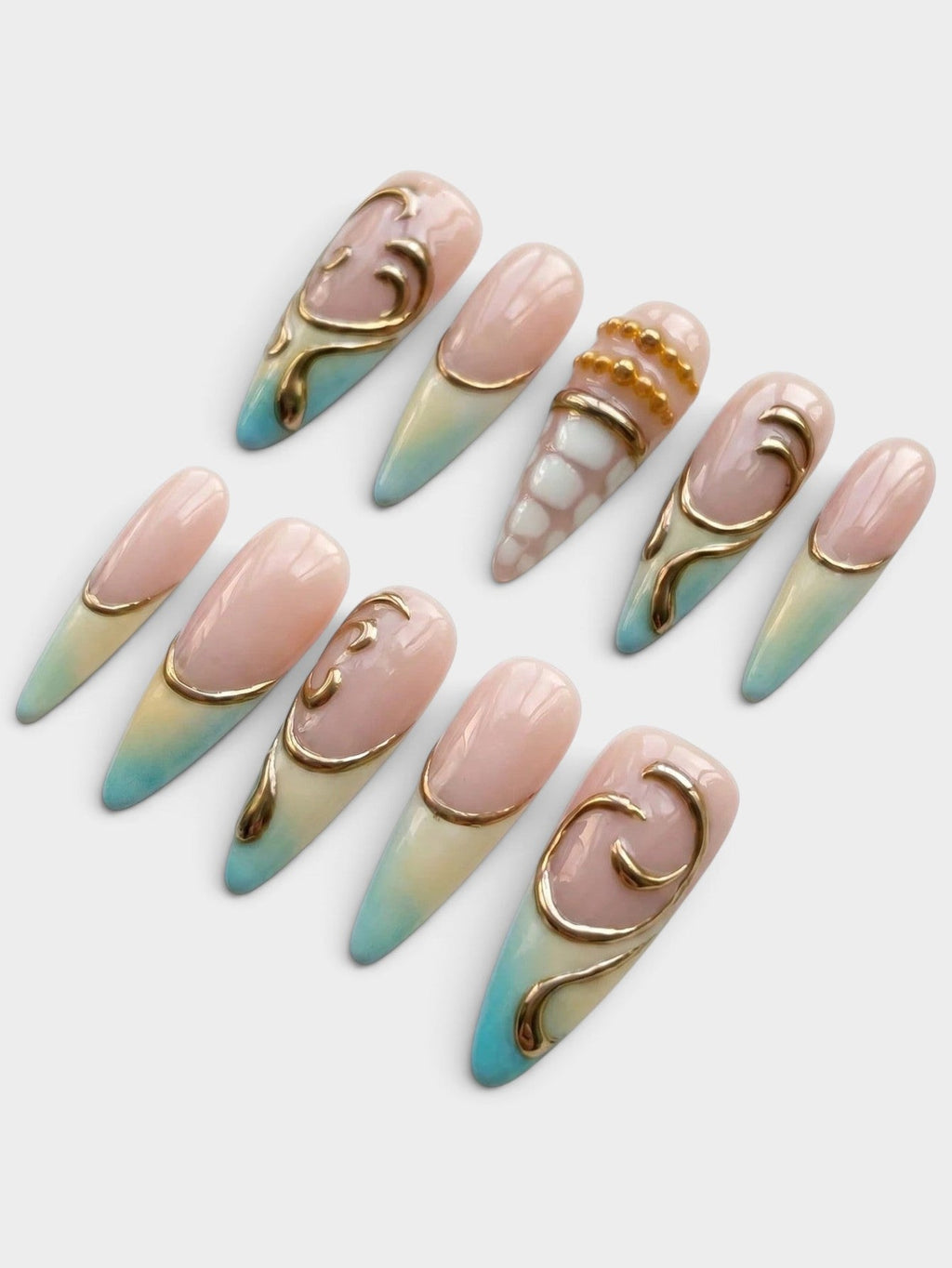 Set de 10 faux ongles Cherry Rouge Gilded Tides en forme amande, dégradé bleu et nude avec motifs dorés en relief.