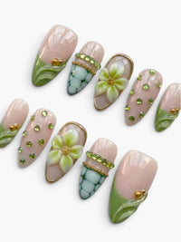 Faux ongles Cherry Rouge en amande nude rosé avec fleurs en relief, strass verts et détails dorés, finition gel