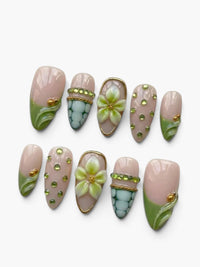 Set de 10 faux ongles Cherry Rouge en amande, base nude rosée avec motifs floraux en relief, strass et détails verts.