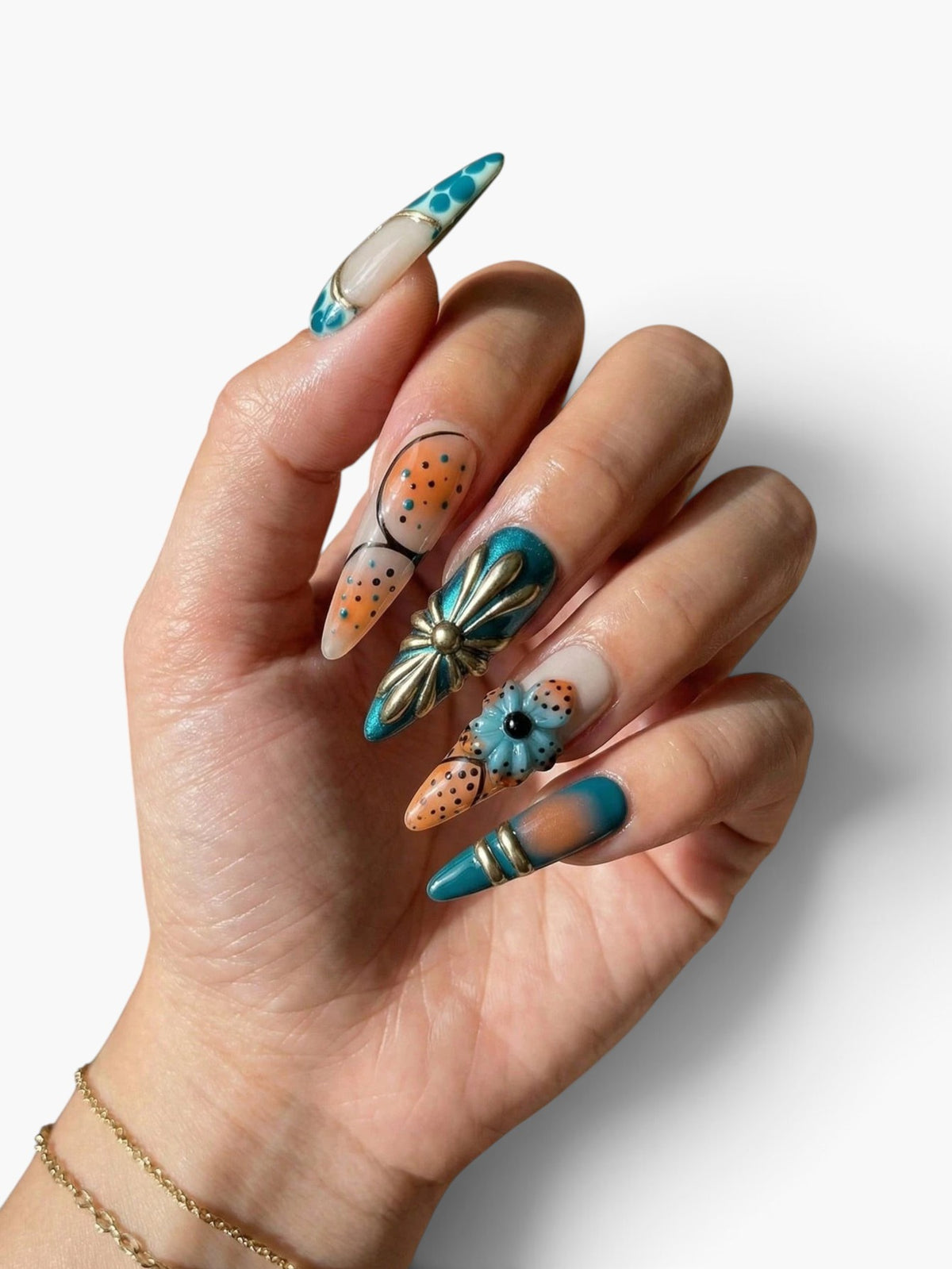 Main Cherry Rouge portant des faux ongles amande avec nail art floral rétro, accents métalliques et tons bleu vert