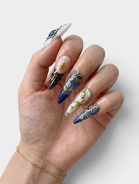 Main Cherry Rouge She’s Royal avec faux ongles pointus en gel bleu marbré, détails dorés en relief et motifs léopard.