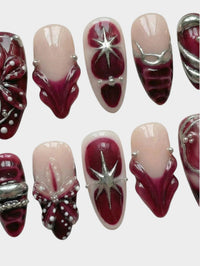 Faux ongles Cherry Rouge Dewdrop Romance avec motifs bordeaux, détails argentés en relief et étoiles scintillantes.