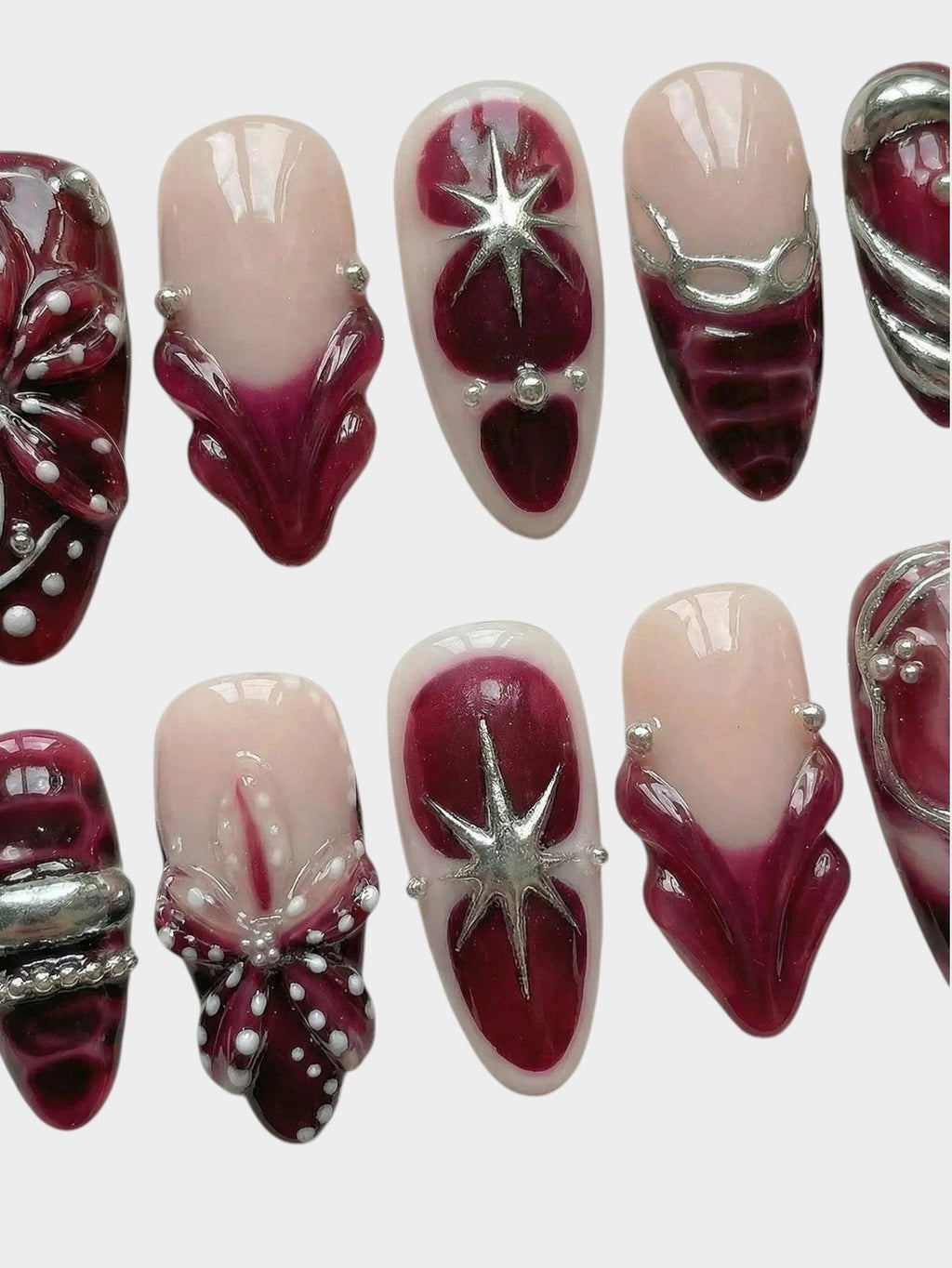 Faux ongles Cherry Rouge Dewdrop Romance avec motifs bordeaux, détails argentés en relief et étoiles scintillantes.