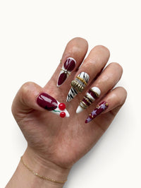 Manucure Cherry Rouge Cherry Mirage en forme amande avec motifs cerises, rayures zébrées, étoiles et bijoux dorés.