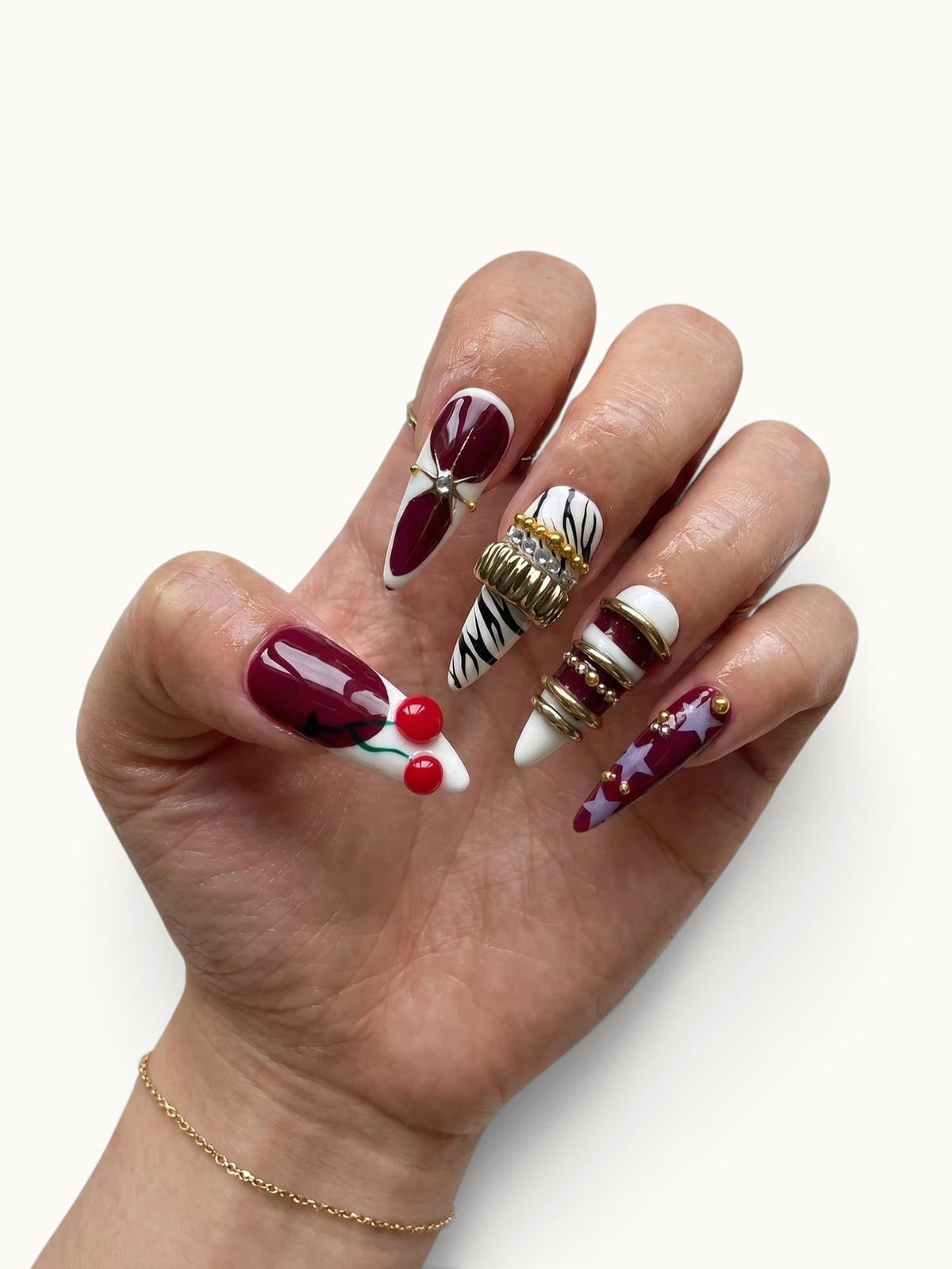 Manucure Cherry Rouge Cherry Mirage en forme amande avec motifs cerises, rayures zébrées, étoiles et bijoux dorés.