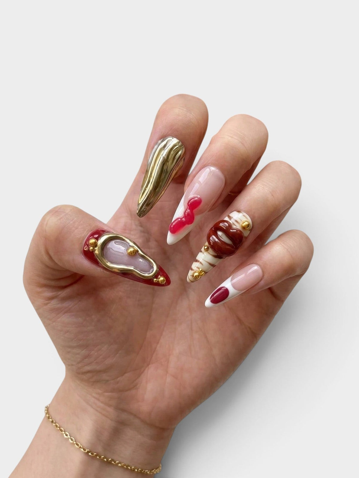 Manucure Cherry Rouge artistique en forme amande avec détails 3D dorés, effets texturés et motifs lèvres sur fond blanc
