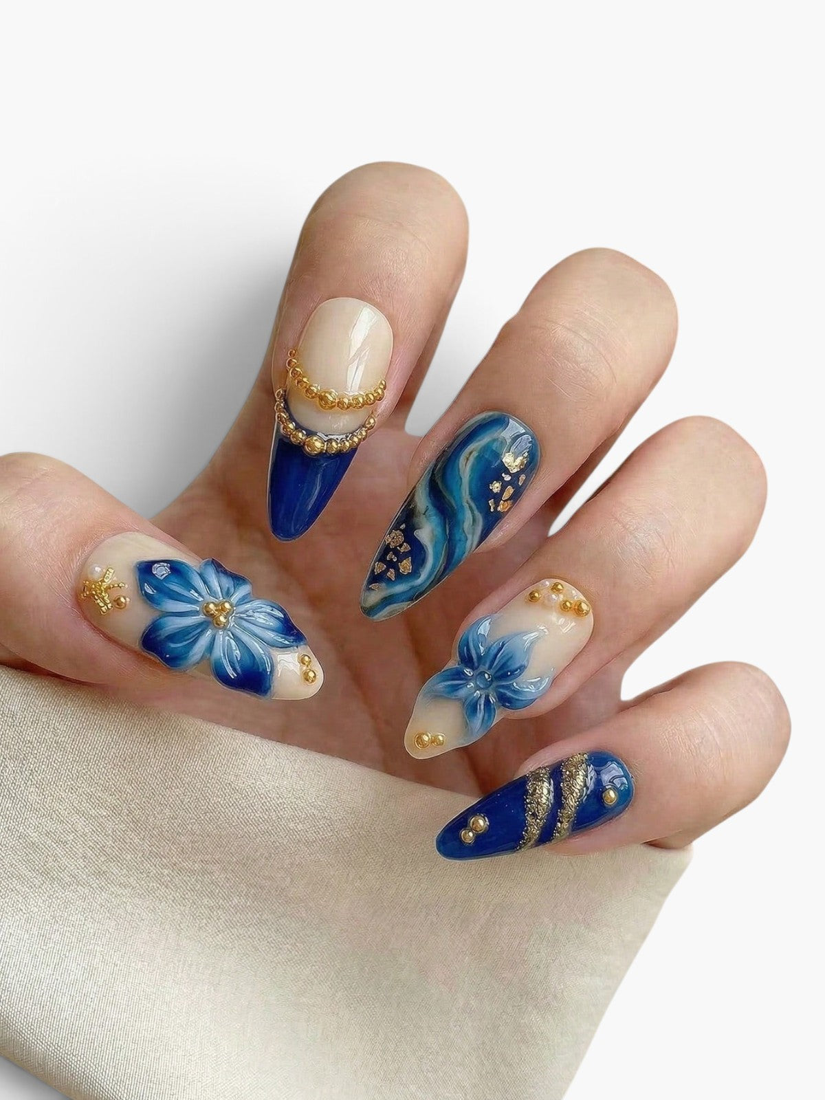 Manucure Cherry Rouge Blue Majesty ovale avec fleurs 3D bleues, perles dorées et motifs effet porcelaine sur gel