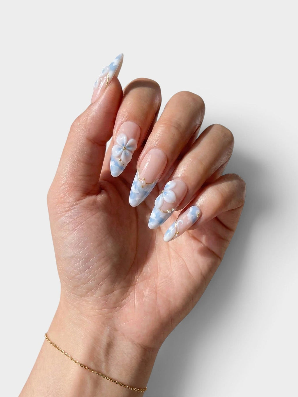 Manucure Cherry Rouge en forme amande avec fleurs 3D bleu ciel et blanc, détails dorés et strass sur ongles longs