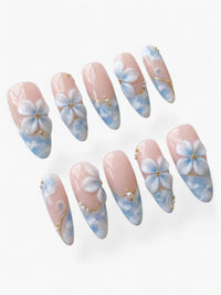 Press-on nails Cherry Rouge en amande avec fleurs sculptées 3D, détails dorés et effet nuage bleu sur fond nude