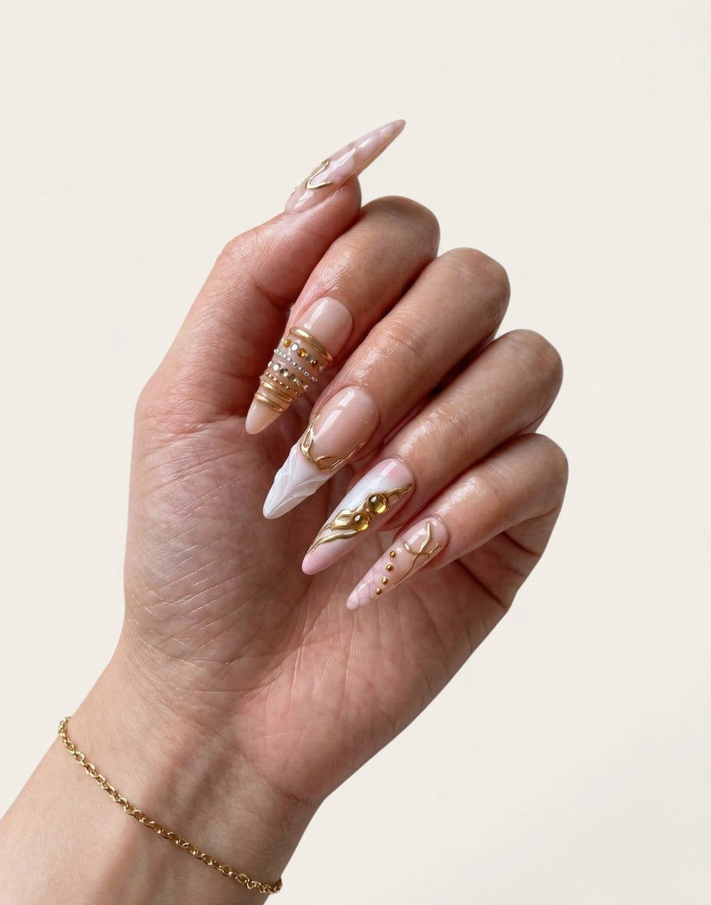 Main Cherry Rouge portant des faux ongles en gel forme amande, design nude irisé, rose pâle avec détails dorés