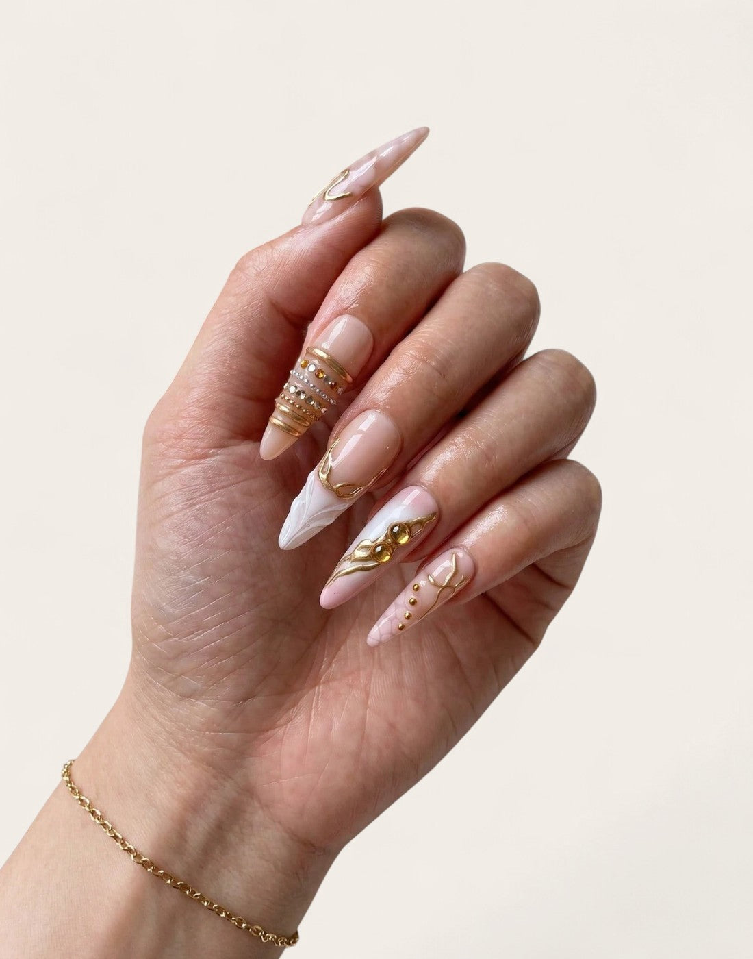 Main Cherry Rouge portant des faux ongles en gel forme amande, design nude irisé, rose pâle avec détails dorés