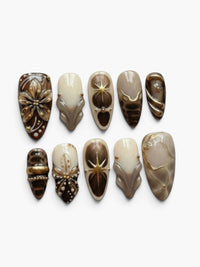 Press-on nails Cherry Rouge Dewdrop Romance Brown en forme amande avec motifs dorés, noirs et effets translucides.